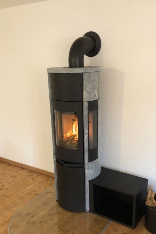 Kaminofen mit Specksteinseiten und Holzfach auf einer Glasbodenplatte
